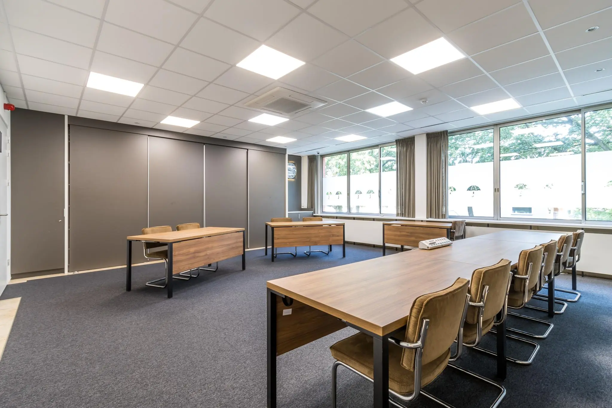 Licht en ruim vergaderlokaal aan de Jan van Eycklaan met houten tafels, comfortabele stoelen en grote ramen met zicht op groen.